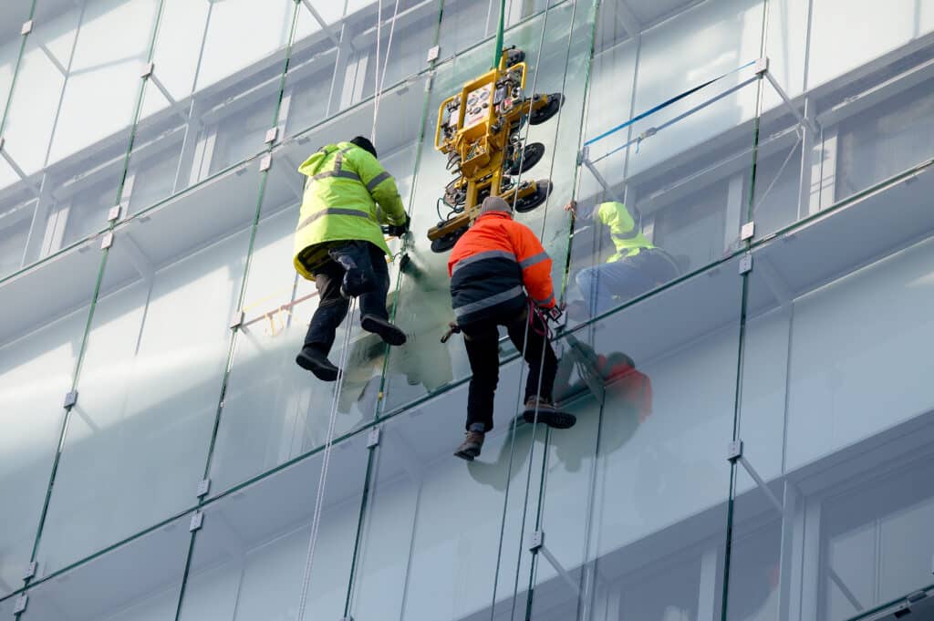 Drei Arbeiter, die eine Scheibe in einer Glasfassade ersetzen