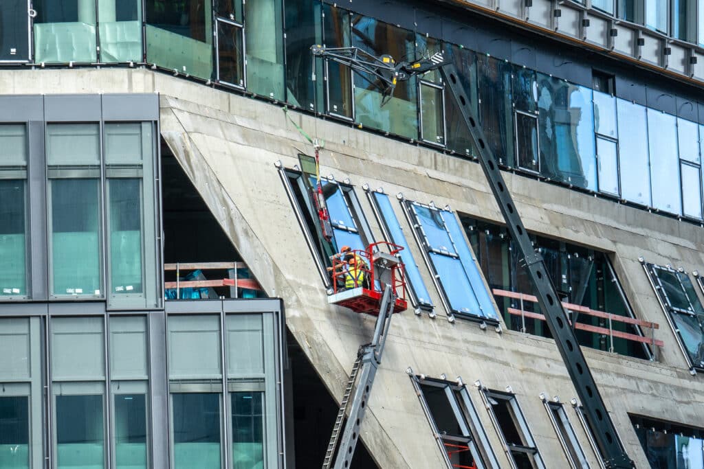 Arbeiter auf Hubarbeitsbühne bei der Fenstermontage an einem Hochhaus